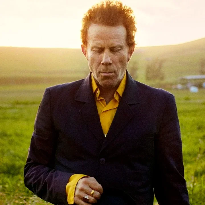 Tom Waits standing in a field at sunset